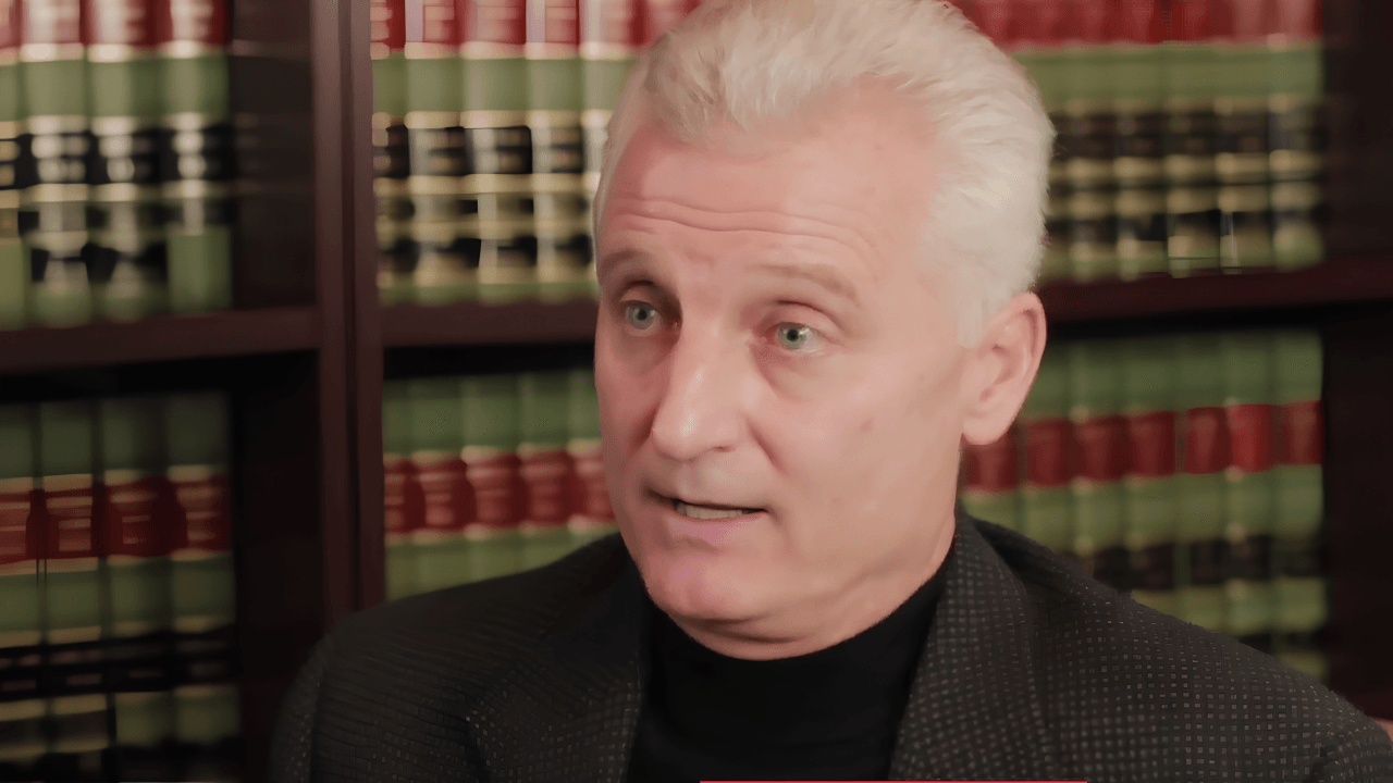 Silver-haired male attorney speaking in front of law library bookshelf